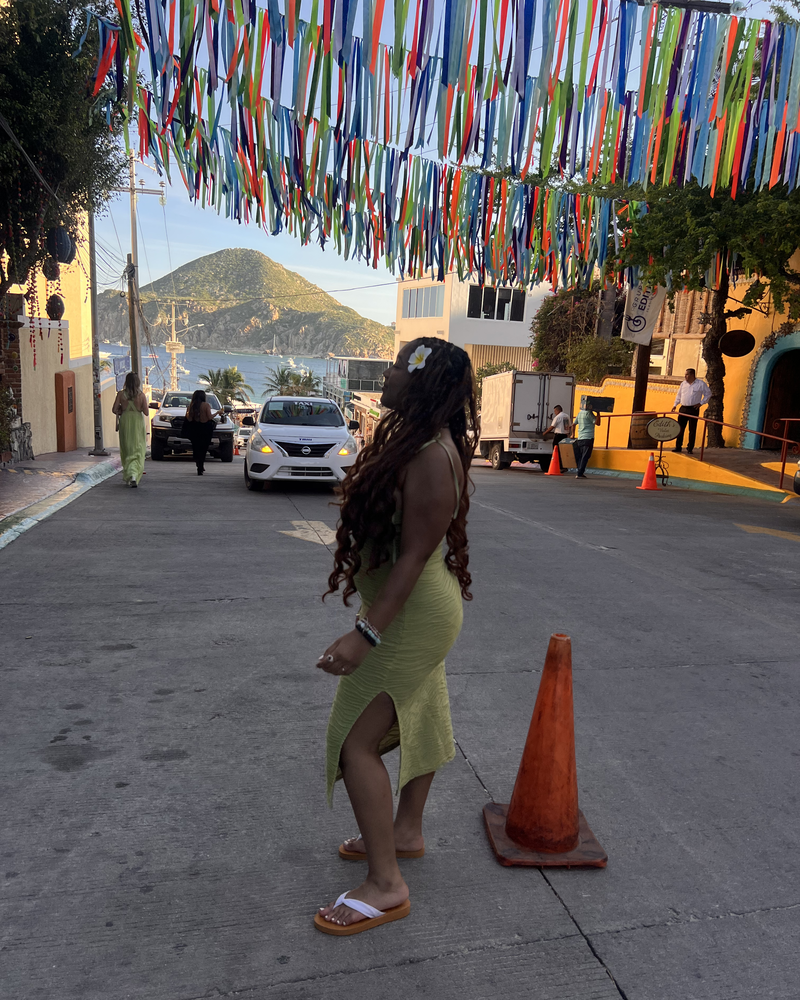 Kymari walking under strings of colorful ribbon on a hillside street in Cabo San Lucas, Mexico