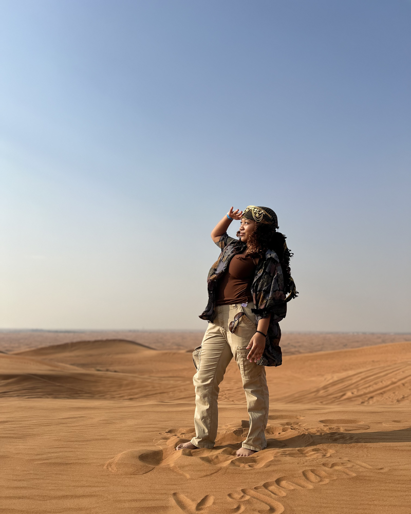 Kymari standing on a desert sand dune, with her name written in the sand